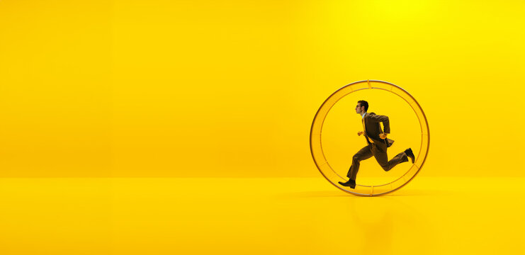 un homme en costume qui court dans une roue g&eacute;ante pour hamster - fond jaune