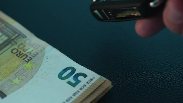 Giving a car key next to a stack of money. Close-up, shallow dof.