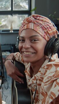 Vertical UGC POV footage of African American female guitarist talking on camera and filming blogger content after recording musical podcast in studio