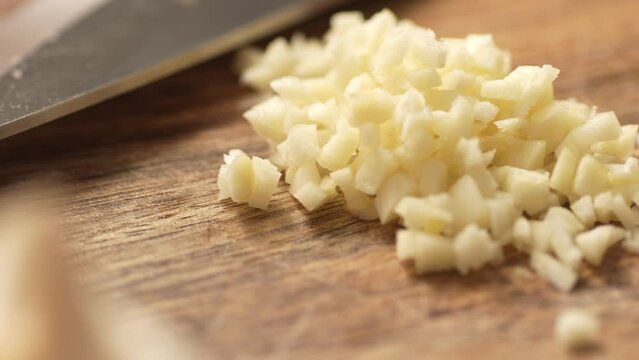 Chopping garlic on a cutting board. Fried Assassin's Spaghetti Cooking Step. Close-up, shallow dof.