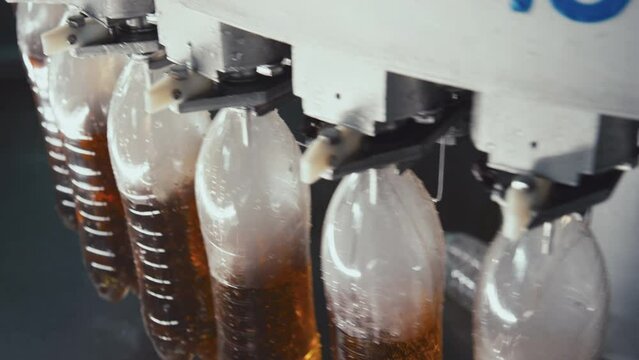 No people high angle closeup of rotating bottle filling industrial machine pouring fizzy drink into plastic bottles at beverage factory