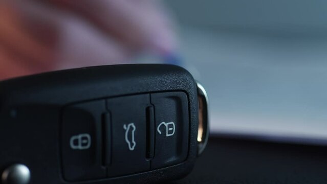 Hand fills in the document next to the car key, then takes it away. Close-up, shallow dof.