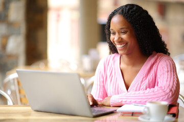 Happy black student using personal computer in a bar