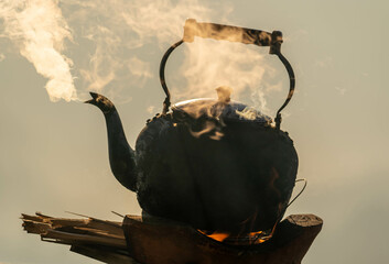 Old kettle on flaming fire with steam boiling water and nature background in morning time