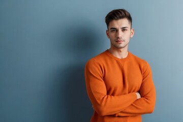 Fototapeta premium Attractive man wearing an orange sweater standing with arms crossed on the blue color background