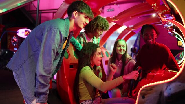 group of multiracial friends having fun playing video arcade and dancing in a night room with neon lights
