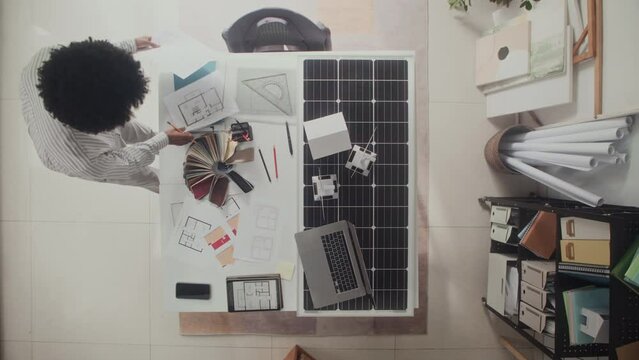 Top view of African American architect working on home interior project at office table with blueprints and solar panel