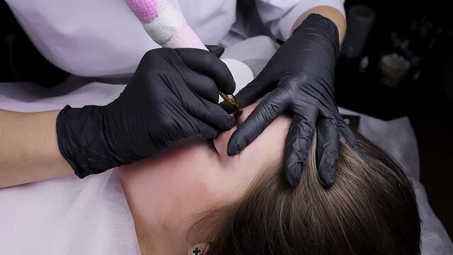 The permanent makeup artist gets to work and perform eyebrow tattooing. Permanent makeup procedure, performing PMU of eyebrows