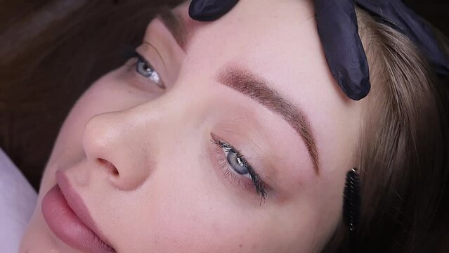 Performed work on permanent eyebrow makeup, the master brushes the hairs after the procedure with a brush. Permanent makeup procedure, performing PMU of eyebrows