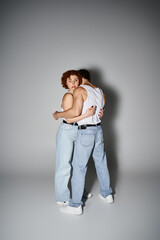 appealing boyfriend and girlfriend in casual attire hugging lovingly on gray backdrop, sexy couple