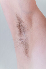 Closeup of long dark hair growing under arm of young female. Concept of hygiene, natural beauty, feminity and body hair growth