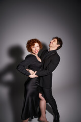 cheerful beautiful woman in black dress smiling at camera next to her joyful laughing boyfriend