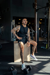 Fototapeta na wymiar Chico joven tatuado y musculoso posando en gimnasio sin camiseta y con ropa moderna