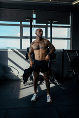 Fototapeta na wymiar Chico joven tatuado y musculoso posando en gimnasio sin camiseta y con ropa moderna