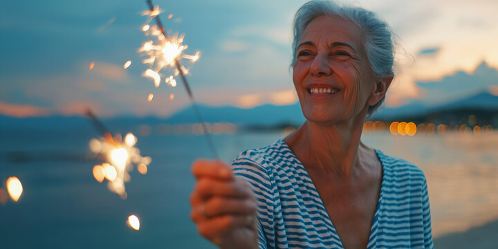 Patriotic elderly woman celebrating fourth of july, wearing striped shirt and holding sparkler fireworks outside at lakeshore - Powered by Adobe