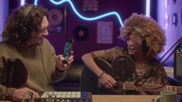 UCC footage of African American lady singing to guitar and looking at smartphone camera while recording video for blogger content at home studio with neon light strings at night