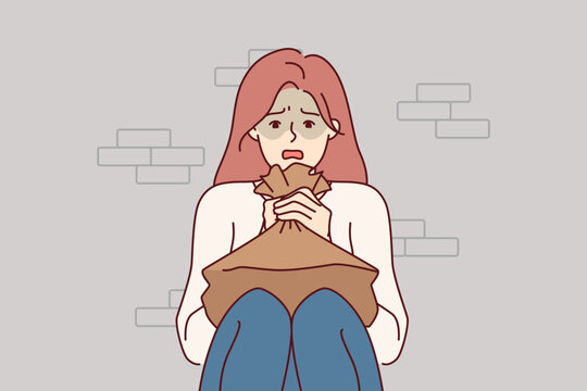 Woman suffering from panic attack holds paper bag for hyperventilation and restoration of normal psychological state. Girl sitting on floor near brick wall and experiencing stress due to panic attack