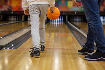 Rear view of teenager boy and father holding bowling ball while standing in bowling alley in...