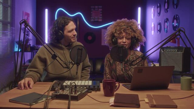 UGC footage of diverse co-hosts hosting video blog with professional equipment at home studio with neon string lights at night