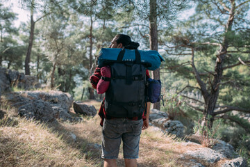 A male tourist with a large backpack and equipment on a mountain trail among the trees.