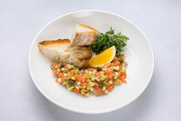 Salmon tartare with tomato and arugula on white plate