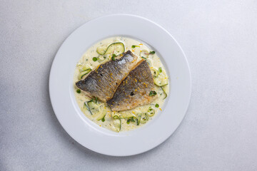 Baked fish with zucchini and dill on a white plate
