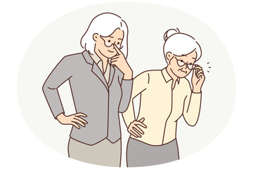 Two elderly women in business clothes carefully look to side watching work of young employees