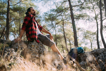 Naklejka premium A male tourist on a hiking trip rests at a halt in a pine forest on a sunny day.