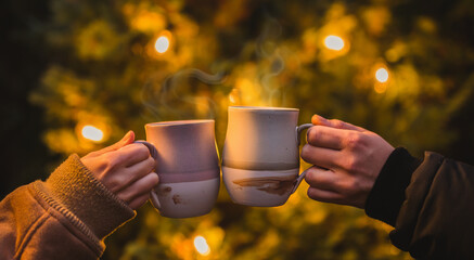 Two mugs clinking together in a winter setting, illuminated by beautiful light and surrounded by a...
