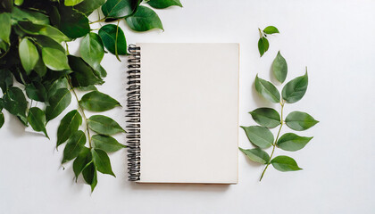 Blank white mockup sketchbook on white background, free space. Top view on empty rustic style notepad with green leaves on table, copy space for text or advertisement.