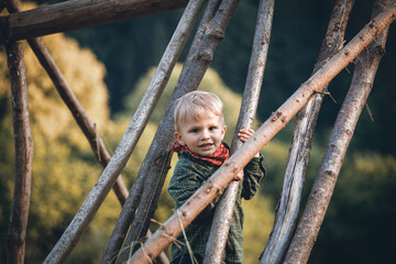 Little Cute Blond Boy Hiding between Wooden Logs - 745786558