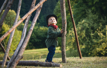 Little Cute Blond Boy in a Hat in Nature between Wooden Logs - 745786731