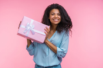 Studio portrait of beautiful confident happy smiling young woman posing with decorated present box in hands isolated over pastel pink background