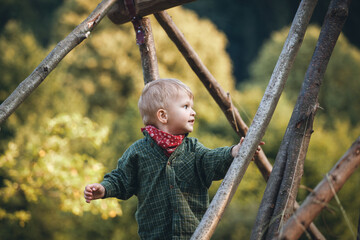 Little Cute Blond Boy in Nature between Wooden Logs - 745786903