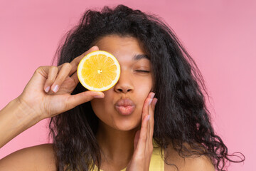 Close up studio shot of beautiful coquette girl posing over pastel pink background with a lemon cut in a half in hand