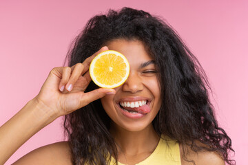 Close up studio portrait of beautiful smiling young woman posing over pastel pink background with a lemon cut in a half in hand - 745787163