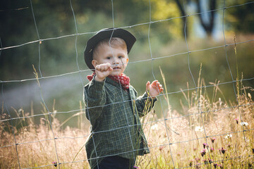 Cute Toddler Kid in Western Cowboy Outfit behind the Wire Fence - 745787345