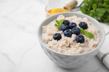 Delicious barley porridge with blueberries and mint in bowl on white marble table, closeup. Space for text