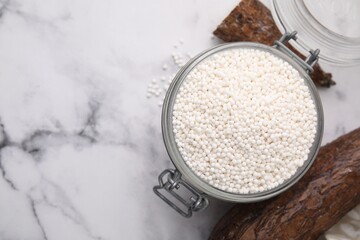 Tapioca pearls in jar and cassava roots on white marble table, flat lay. Space for text
