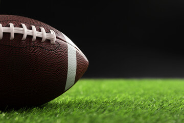 Rugby ball on green grass against black background, closeup. Space for text