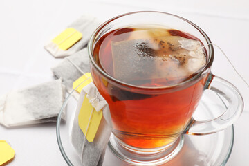Tea bags and cup of aromatic drink on white table, closeup