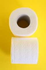 Soft toilet paper rolls on yellow background, top view