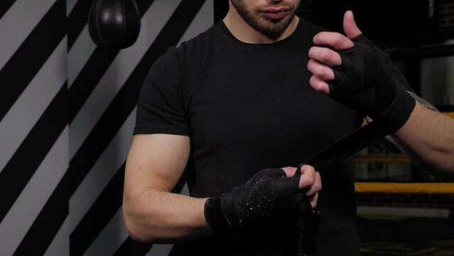 Close-up of a man wrapping a black bandage around his wrists, preparing for boxing training.