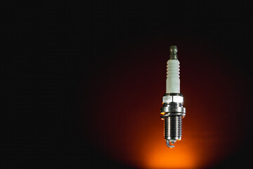 Spark plug isolated on black and orange background. Spare part for a vehicle with an internal...