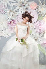 Beautiful young bride in an elegant dress on a background of a large paper flowers.