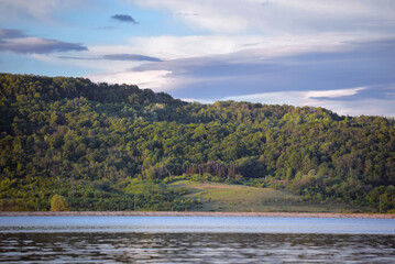 A large lake with calm waters at the edge of a picturesque tall forest in a village far from the cities