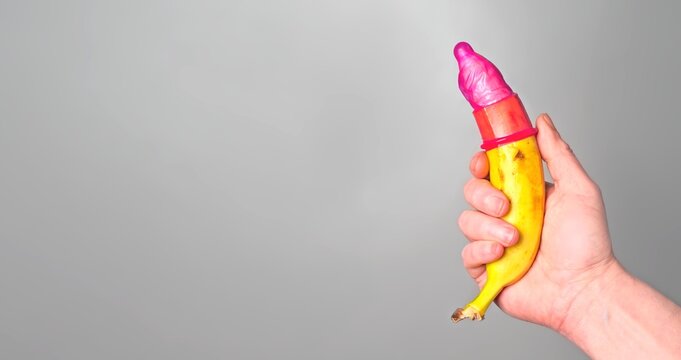 Unrecognizable person holding a banana with Red condom. Panoramic image with copy space. Safe sex concept.
