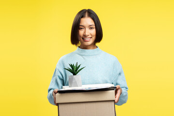 Portrait of smiling young asian woman holding box with things and flower pot, fired from work