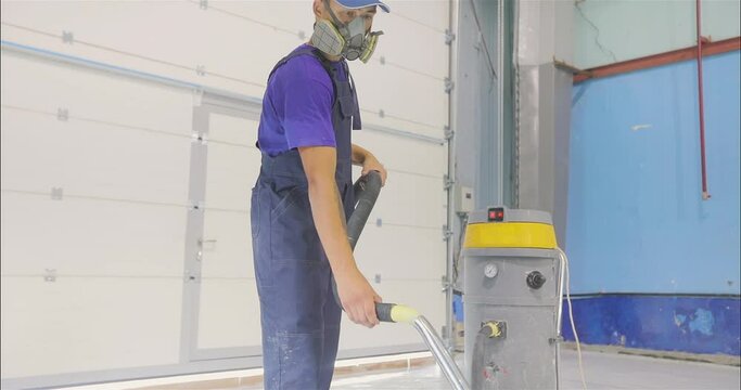 A builder cleans the construction site of dust using a construction vacuum cleaner. cleaning the construction site from dust. The process of vacuuming a polymer floor after finishing work