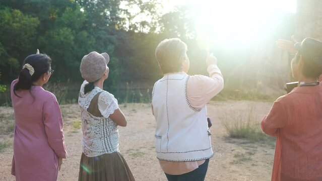 Group of healthy senior, pensioners, elderly female friends share experiences laughter standing against sunlight meadow enjoy a rustic countryside, happy adventures in retirement traveling lifestyle